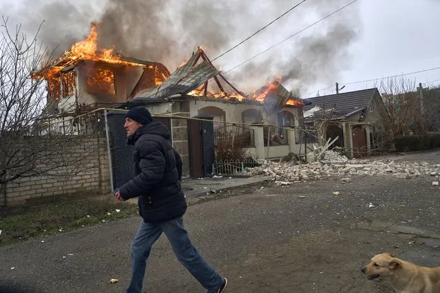 A local resident runs past a burning house hit by the Russian shelling in Kherson, Ukraine, on the Orthodox Christmas Eve Friday, January 6, 2023. (Photo by LIBKOS/AP Photo)