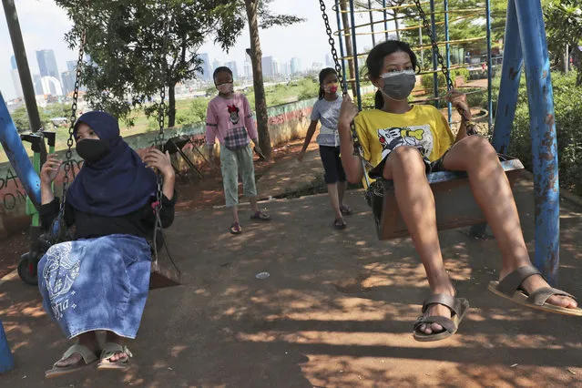 Indonesian children wearing face masks as a precaution against coronavirus outbreak play on swings in Jakarta, Indonesia, Wednesday, September 23, 2020. (Photo by Tatan Syuflana/AP Photo)