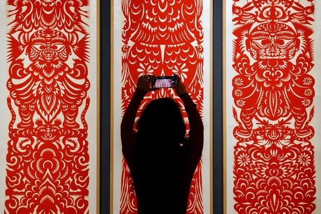 A woman takes a smartphone photo of the Chinese traditional paper cutting arts exhibited at the Beijing Art and Craft Museum during the Lunar New Year celebrations in Beijing, Sunday, January 29, 2023. Chinese people are enjoying a week-long holiday for the Lunar New Year and visiting various temple fairs and exhibitions held in the cities around China. (Photo by Andy Wong/AP Photo)