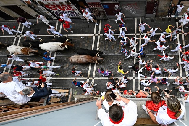 Participants run ahead of bulls during the first “encierro” (bull-run) of the San Fermin festival in Pamplona, northern Spain, on July 7, 2025. Thousands of people every year attend the week-long festival and its famous 'encierros': six bulls are released at 8:00 a.m. evey day to run from their corral to the bullring through the narrow streets of the old town over an 850 meters (yard) course while runners ahead of them try to stay close to the bulls without falling over or being gored. (Photo by Ander Gillenea/AFP Photo)
