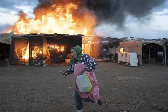 A woman runs past burning shacks during a fire before an eviction by police officers in Almeria, Spain, Monday, January 30, 2023. A migrant camp in southern Spain's town of Nijar that was set to be demolished Monday has caught fire. Over 400 people live there, many working as temporary workers in farming estates. (Photo by Santi Donaire/AP Photo)