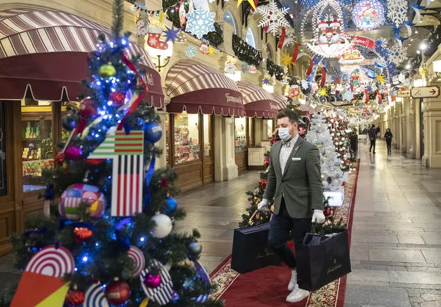 In this Monday, November 23, 2020 file photo, a man wearing face mask and gloves to protect against coronavirus carries purchases among as the GUM State Department store is decorated for Christmas and New Year celebrations in Moscow, Russia. Nations are struggling to reconcile cold medical advice with a holiday tradition that calls for big gatherings in often poorly ventilated rooms, where people chat, shout and sing together, providing an ideal conduit for a virus that has killed over 350,000 people in Europe so far. (Photo by Pavel Golovkin/AP Photo/File)