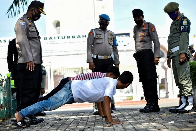 Members of the public perform push-ups as punishment for not wearing face masks amid the Covid-19 coronavirus pandemic in Banda Aceh on November 10, 2020. (Photo by Chaideer Mahyuddin/AFP Photo)
