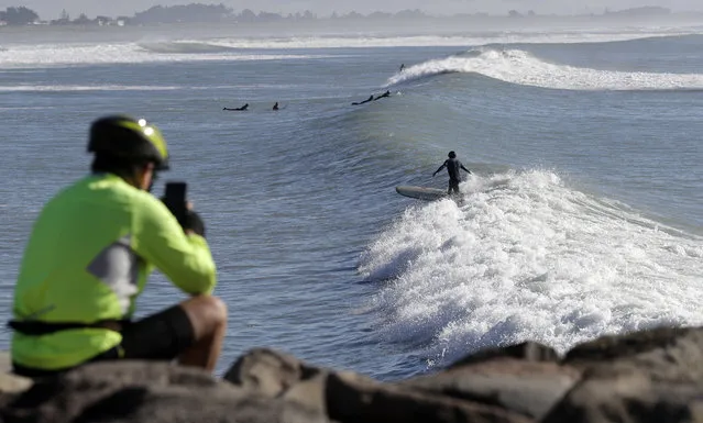 A spectator photographs surfers at Sumner Beach near Christchurch, New Zealand, Tuesday, May 1, 2018. Surfers enjoyed smooth one meter waves at the popular beach on the outskirts of Christchurch. (Photo by Mark Baker/AP Photo)