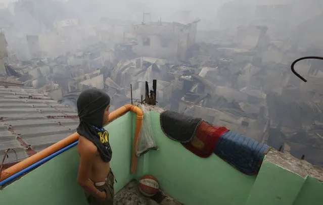 A boy looks at houses gutted by a fire from a partially damaged house at a slum colony in Quezon city, Metro Manila January 1, 2015. (Photo by Erik De Castro/Reuters)