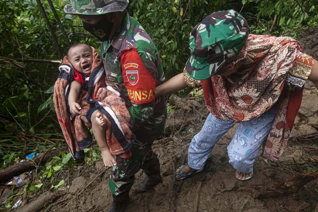 An Indonesian soldier assists a woman to carry her baby as they make their way through an area affected by earthquake-triggered landslide near Mamuju, West Sulawesi, Indonesia, Saturday, January 16, 2021. (Photo by Yusuf Wahil/AP Photo)