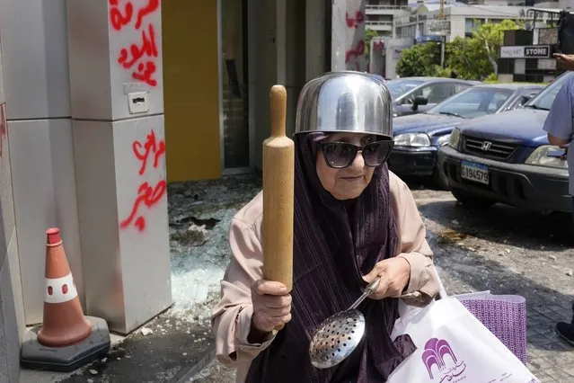 A woman with a pot on her head holds a rolling pin and ladle, protests outside Byblos Bank during a protest demanding the release of depositors' trapped savings, in Beirut, Lebanon, Thursday, June 15, 2023. (Photo by Hussein Malla/AP Photo)