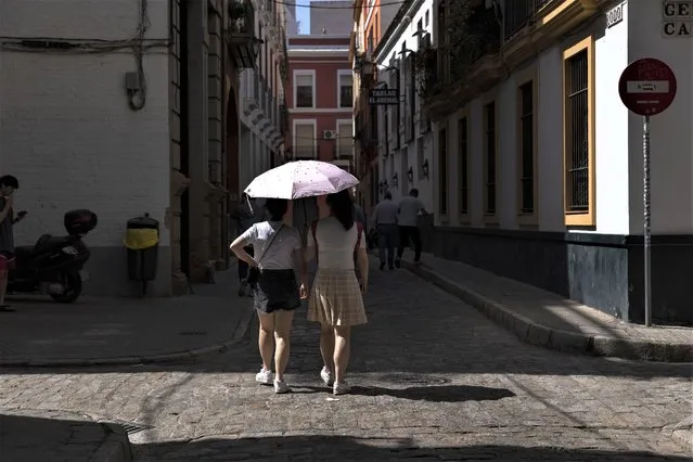 A couple share a sun umbrella in the streets of Seville, Spain, April 27, 2023. Record-breaking April temperatures in Spain, Portugal and northern Africa were made 100 times more likely by human-caused climate change, a new flash study found. (Photo by Santi Donaire/AP Photo)