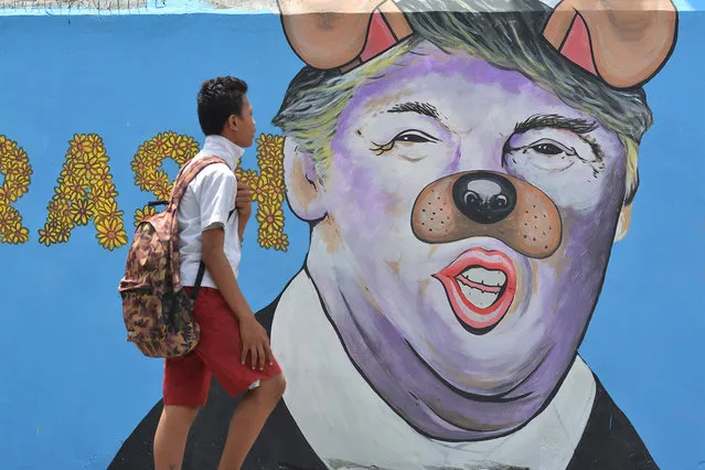 A student passes in front of a mural depicting US President Donald Trump with a nose and ears like a dog at Palu on February 27, 2017 in Central Sulawei, Indonesia. (Photo by Sijori Images/Barcroft Images)