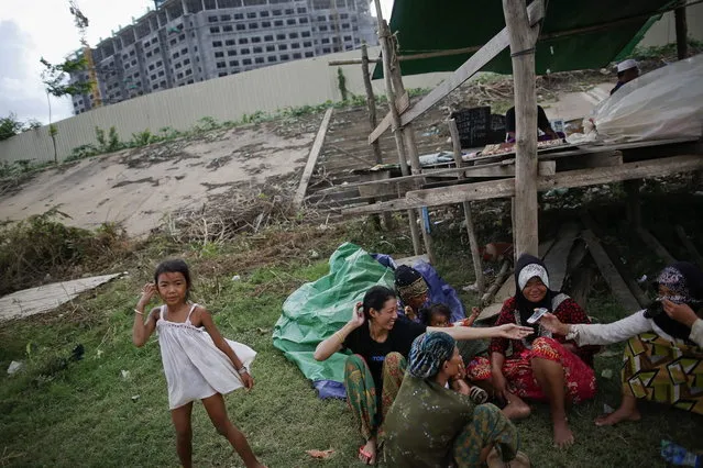 Ethnic Cham Muslim women chat near a makeshift mosque built in front of a hotel under construction on the banks of Mekong river in Phnom Penh July 27, 2013. About 100 ethnic Cham families, made up of nomads and fishermen without houses or land who arrived at the Cambodian capital in search of better lives, live on their small boats on a peninsula where the Mekong and Tonle Sap rivers meet, just opposite the city's centre. The community has been forced to move several times from their locations in Phnom Penh as the land becomes more valuable. They fear that their current home, just behind a new luxurious hotel under construction at the Chroy Changva district is only temporary and that they would have to move again soon. (Photo by Damir Sagolj/Reuters)