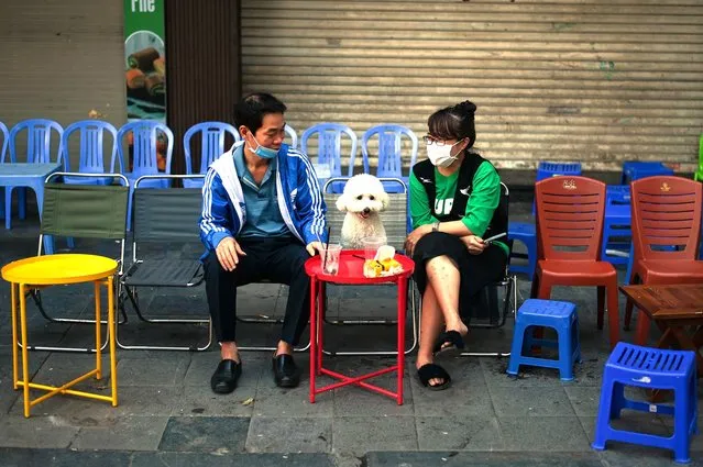 A couple sits with their dog at a streetside coffee stall near the popular Hoan Kiem lake during the Lunar New Year or Tet holiday in Hanoi on February 14, 2021. (Photo by Manan Vatsyayana/AFP Photo)