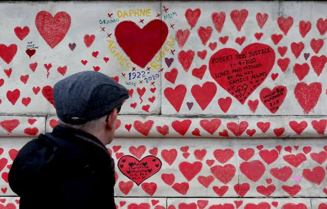 A man walks past the National Covid Memorial Wall commemorating all those who have died of coronavirus, on the Thames Embankment opposite the Houses of Parliament in London, Thursday, April 8, 2021. Bereaved families want the wall of painted hearts to remain a site of national commemoration and are asking the Prime Minister to help make the memorial permanent. (Photo by Frank Augstein/AP Photo)