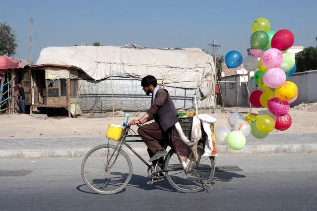 An Afghan balloon vendor rides a bicycle along a street in Kabul on August 31, 2023. (Photo by Wakil Kohsar/AFP Photo)