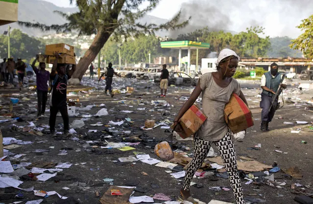 People carry merchandise from the Delimart supermarket complex which was burned during  two days of protests against a planned hike in fuel prices in Port-au-Prince, Haiti, Sunday, July 8, 2018. Government officials had agreed to reduce subsidies for fuel as part of an assistance package with the International Monetary Fund, but the government suspended the fuel hike after widespread violence broke out. (Photo by Dieu Nalio Chery/AP Photo)