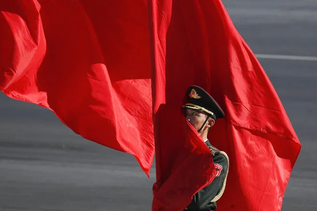 A member of a Chinese honor guard is partially covered with red flags as he waits for the arrival of Japanese Prime Minister Shinzo Abe during a welcome ceremony outside the Great Hall of the People in Beijing, Friday, October 26, 2018. (Photo by Andy Wong/AP Photo)
