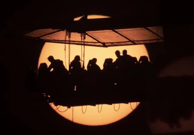 People have dinner sitting on a platform raised by a crane to a height of 50 meters and silhouetting against the sun as they participate the traveling international project “Dinner in the Sky” in St. Petersburg, Russia, Wednesday, June 2, 2021. (Photo by Dmitri Lovetsky/AP Photo)