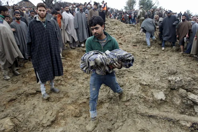 A man carries the body of a child after it was pulled out from the rubble after a hillside collapsed onto a house at Laden village, west of Srinagar, March 30, 2015. Army and police used shovels and diggers to locate any survivors. (Photo by Danish Ismail/Reuters)