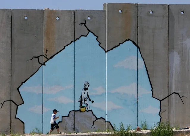 A Palestinian boy walks past a creation by Banksy along part of the controversial Israeli barrier near the Kalandia checkpoint in the West Bank in 2005. (Photo by Reuters/Stringer)