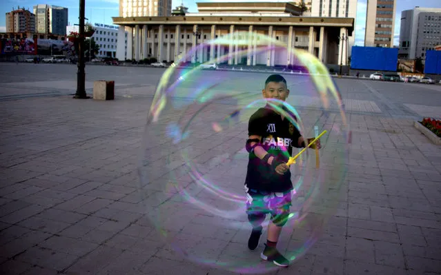 A boy plays with a bubble on the main square next to the Mongolian Parliament House in Ulan Bator on July 1, 2016. (Photo by Johannes Eisele/AFP Photo)