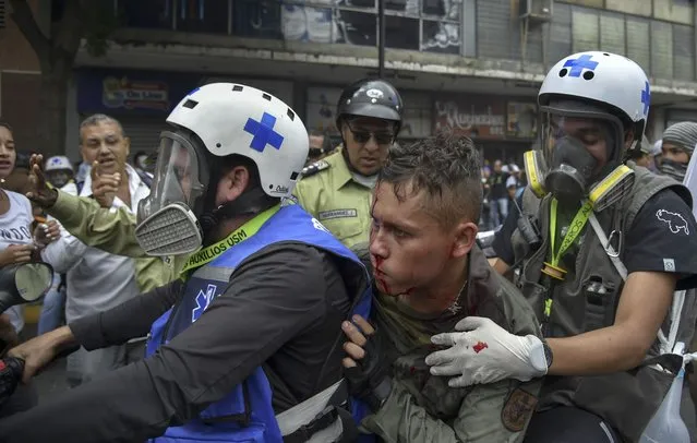 Paramedics rescue a wounded member of the Bolivarian National Guard during clashes with opposition demonstrators, in a protest against the government of President Nicolas Maduro on the anniversary of the 1958 uprising that overthrew the military dictatorship, in Caracas on January 23, 2019. (Photo by Yuri Cortez/AFP Photo)