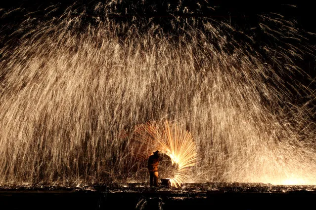Chinese traditional folk performer spray the molten iron against a cold stone city wall to create sparks imitated as the fireworks to celebrate the upcoming Chinese traditional Lantern Festival in Nuanquan Town, rural Zhangjiakou city, China's Hebei province, February 21, 2016. Chinese traditional Lantern Festival will fall on 22 February that as one of the most important festivals in China, marks the end of the lunar new year celebrations and is traditionally celebrated by viewing lanterns and guessing lantern riddles and so on. (Photo by Wu Hong/EPA)