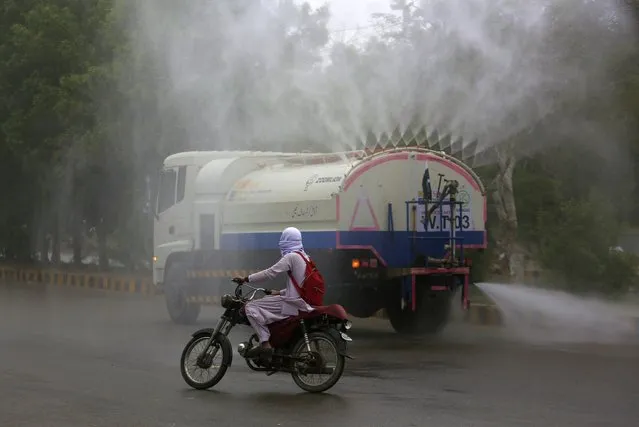 A motorcyclist rides past a tanker spraying disinfectant in an effort to contain the outbreak of the coronavirus, in Karachi, Pakistan, Saturday, August 14, 2021. (Photo by Fareed Khan/AP Photo)