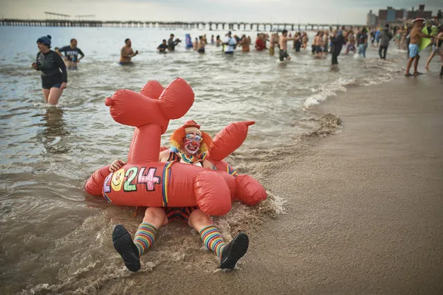 A clown lies on the beach as revelers enter the cold water during the annual Polar Bear Plunge, Monday, January 1, 2024, in New York. (Photo by Andres Kudacki/AP Photo)