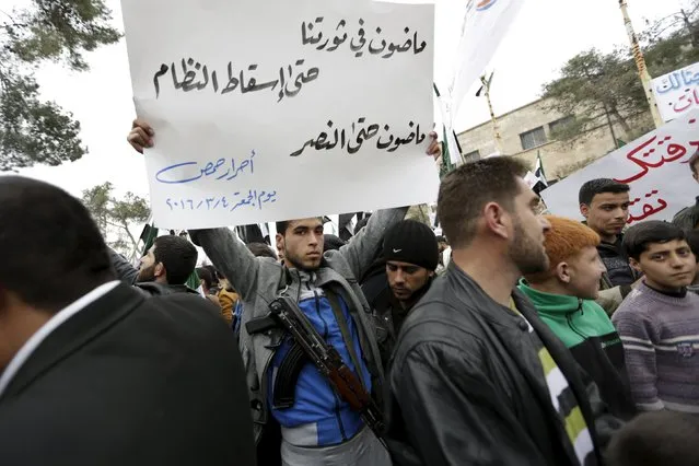 A rebel fighter carries a banner during an anti-government protest in the town of Marat Numan in Idlib province, Syria March 4, 2016. The text on the banner reads in Arabic: “We are continuing in our revolution, till the fall of the regime, we are continuing till victory; The Free people of Homs”. (Photo by Khalil Ashawi/Reuters)