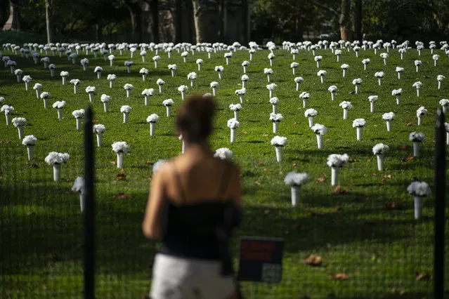 A woman looks at vases of white flowers that are part of an installation of 1,050 representing the lives lost by gun violence in New York the previous year, displayed in New York's Battery Park, Thursday, October 7, 2021. The governors of four northeastern states agreed Thursday to share information about firearms purchases to help detect and investigate straw buyers and other gun crimes. (Photo by Eduardo Munoz Alvarez/AP Photo)