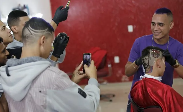 People take pictures of hair artist and barber Nariko, 27, and his work on customer Luiz Fernadez, 15, an image of Barcelona's Neymar and his team's badge shaved on his head, before the Champions League semifinal first leg soccer match between Barcelona and Bayern Munich at a barbershop in Sao Vicente, near Santos, in Sao Paulo state May 6, 2015. (Photo by Nacho Doce/Reuters)