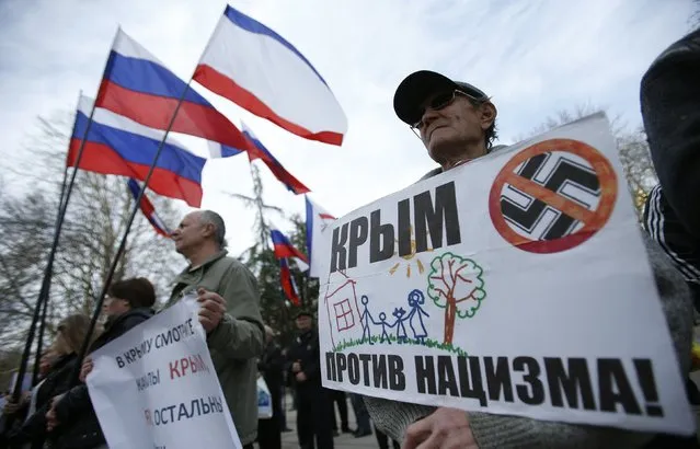 A man holds a banner as he attends a pro-Russian rally at the Crimean parliament building in Simferopol March 6, 2014. The decree making Crimea part of Russia is already in force and Ukrainian troops still on its territory will be treated as occupiers and forced to surrender or leave, the Russian-controlled region's deputy prime minister said. The banner reads “Crimea is Against Nazism”. (Photo by David Mdzinarishvili/Reuters)