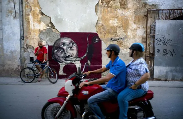 In this February 9, 2017 photo, graffiti artist Yulier Rodriguez Perez poses with one of his works, painted on a wall in Old Havana, Cuba. Rodriguez was born in the central province of Camagüey, where he says he tried without success to get a formal art education. He gave up and ended up learning on his own with local teachers. (Photo by Ramon Espinosa/AP Photo)