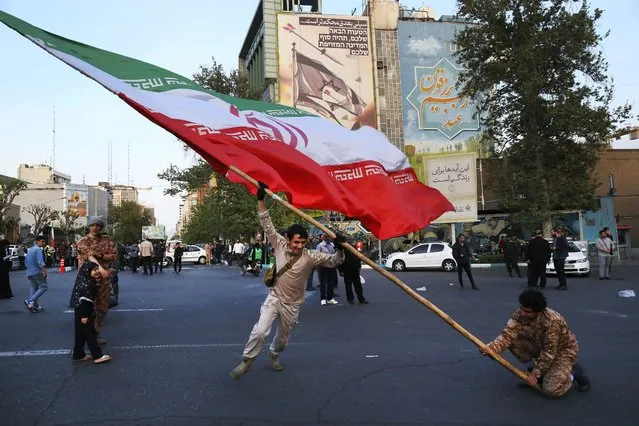 Demonstrators wave a huge Iranian flag in their anti-Israeli gathering in front of an anti-Israeli banner on the wall of a building at the Felestin (Palestine) Sq. in Tehran, Iran, Monday, April 15, 2024. World leaders are urging Israel not to retaliate after Iran launched an attack involving hundreds of drones, ballistic missiles and cruise missiles. The sign on the banner reads in Hebrew: “Your next mistake will be the end of your fake country”. And the sign in Farsi reads: “The next slap will be harder”. (Photo by Vahid Salemi/AP Photo)