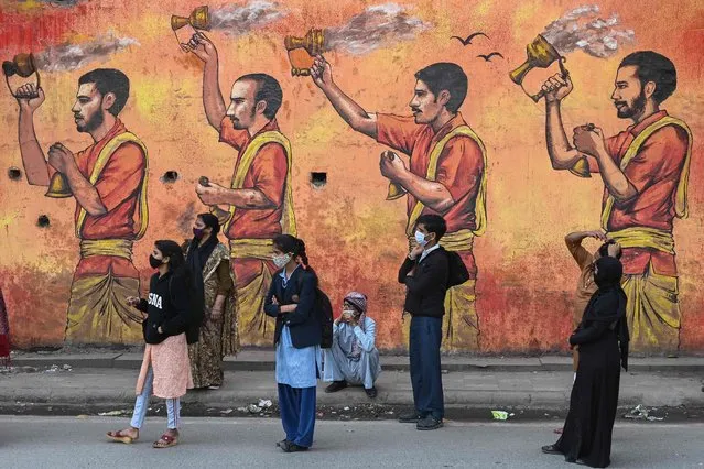 People wait for a bus along a road on the backdrop of a wall mural in New Delhi on February 14, 2022. (Photo by Sajjad Hussain/AFP Photo)