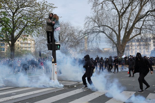 People stand on a pedestrian traffic light during clashes at a demonstration as part of the tenth day of nationwide strikes and protests against French government's pension reform in Paris, France on March 28, 2023. (Photo by Nacho Doce/Reuters)