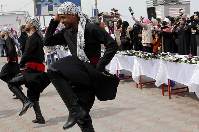 Men wearing traditional costumes perform Dabke, a Levantine folk dance seen at joyous occasions, in front of Palestinian women waving flowers while marking International Women's Day along the Mediterranean Sea in Gaza City, Tuesday, March 8, 2022. (Photo by Adel Hana/AP Photo)
