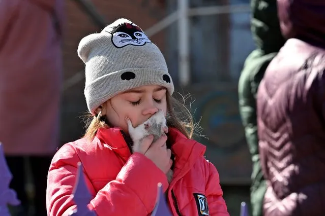 A girl kisses her pet mouse outside a five-storey residential building that partially collapsed after a shelling in Kyiv on March 18, 2022, as Russian troops try to encircle the Ukrainian capital as part of their slow-moving offensive. Authorities in Kyiv said one person was killed early today when a downed Russian rocket struck a residential building in the capital's northern suburbs. They said a school and playground were also hit. (Photo by Sergei Supinsky/AFP Photo)