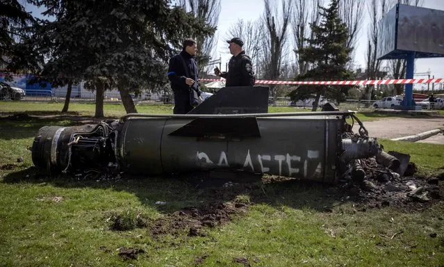 Ukrainian police inspect the remains of a large rocket with the words “for our children” in Russian next to the main building of a train station in Kramatorsk, eastern Ukraine, that was being used for civilian evacuations, that was hit by a rocket attack killing at least 35 people, on April 8, 2022. (Photo by Fadel Senna/AFP Photo)