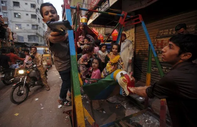 A boy (L) gestures with a toy gun while children play on a swing along a street during Eid al-Fitr, which marks the end of the holy month of Ramadan, in Karachi, Pakistan, July 20, 2015. (Photo by Akhtar Soomro/Reuters)