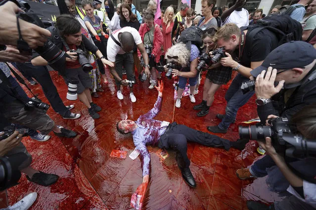 Photographers view the scene as a member of environmental activist group Extinction Rebellion rolls around in fake blood in Paternoster Square, central London, Friday August 27, 2021. Extinction Rebellion protests are aiming to occupy parts of central London, with its declared aim to call for a halt to all new investment in fossil fuels. (Photo by Kirsty O'Connor/PA Wire via AP Photo)