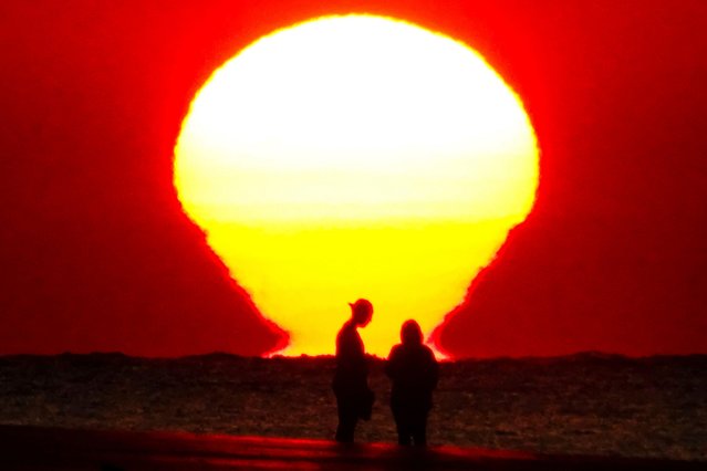 The sun rises over the Atlantic Ocean reflected on the water silhouetting a couple on the beach as a heat wave sweeps across the region bringing temperatures into the 90's, on May 29, 2024 in Isle of Palms, South Carolina. (Photo by Richard Ellis/Alamy Live News)