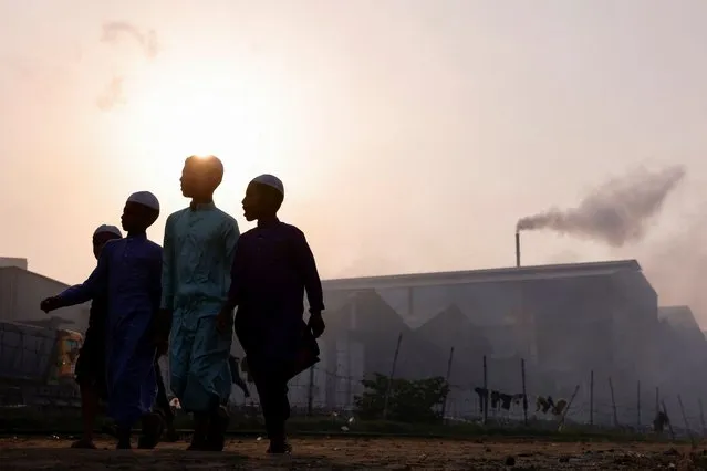 Children walk on the street as smoke rises from a re-rolling mill in Dhaka, Bangladesh, May 16, 2022. (Photo by Mohammad Ponir Hossain/Reuters)