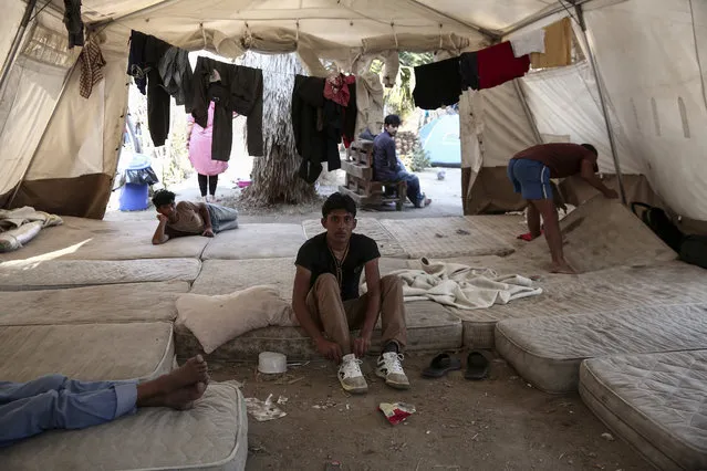 A migrant ties his laces inside a tent which have been set up at the premises of an abandoned hotel where dozens of migrants have been living the last weeks at Kos town, on the southeastern island of Kos, Monday, August 10, 2015. (Photo by Yorgos Karahalis/AP Photo)