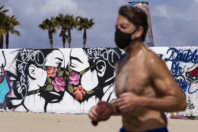 A man wearing a face mask jogs past a mural showing a couple kissing with face masks next to the beach amid the coronavirus pandemic in Venice, California, USA, 28 March 2020. Los Angeles Mayor Eric Garcetti ordered yesterday for all the beaches and trails to be closed to fight against the spread of the epidemic. (Photo by Etienne Laurent/EPA/EFE)