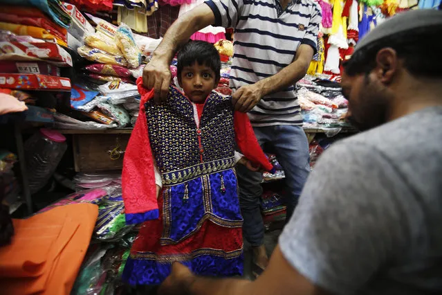 A man holds up a dress for size on a Kashmiri child ahead of Eid al-Fitr in Srinagar, Indian controlled Kashmir Tuesday, July 5, 2016. Eid al-Fitr marks the end of the fasting month of Ramadan. (Photo by Mukhtar Khan/AP Photo)