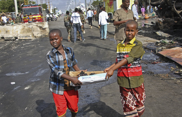 Somali children assist other civilians and security forces in their rescue efforts by carrying away unidentified charred human remains in a cardboard box, to clear the scene of Saturday's blast, in Mogadishu, Somalia, Sunday, October 15, 2017. The death toll from the huge truck bomb blast in Somalia's capital rose to over 50 Sunday, with more than 60 others injured, as hospitals struggled to cope with the high number of casualties, security and medical sources said. (Photo by Farah Abdi Warsameh/AP Photo)