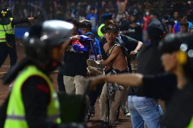 In this picture taken on October 1, 2022, a group of people carry a man at Kanjuruhan stadium in Malang, East Java. At least 127 people died at a football stadium in Indonesia late on October 1 when fans invaded the pitch and police responded with tear gas, triggering a stampede, officials said. (Photo by AFP Photo/Stringer)