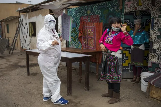 Olinda Silvano from the Shipibo Conibo ethnic group, talks to a member of an NGO dressed in protective gear against the new coronavirus, during the celebration of the feast of Saint John the Baptist, the patron saint of the Peruvian Amazon, in the Cantagallo neighborhood of Lima, Peru, Wednesday, June 24, 2020. The neighborhood reopened about 10 days ago after it had been under strict quarantine due to an outbreak of COVID-19. (Photo by Rodrigo Abd/AP Photo)