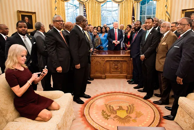 Counselor to the President Kellyanne Conway (L) checks her phone after taking a photo as US President Donald Trump and leaders of historically black universities and colleges pose for a group photo in the Oval Office of the White House before a meeting with Vice President Mike Pence in Washington, DC on February 27, 2017. (Photo by Brendan Smialowski/AFP Photo)