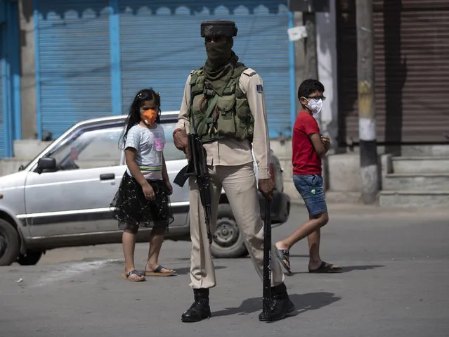 Kashmiri children walk past a paramilitary soldier during curfew in Srinagar, Indian controlled Kashmir, Tuesday, August 4, 2020. Authorities clamped a curfew in many parts of Indian-controlled Kashmir on Tuesday, a day ahead of the first anniversary of India’s controversial decision to revoke the disputed region’s semi-autonomy. Shahid Iqbal Choudhary, a civil administrator, said the security lockdown was clamped in the region’s main city of Srinagar in view of information about protests planned by anti-India groups to mark Aug. 5 as “black day”. (Photo by Mukhtar Khan/AP Photo)